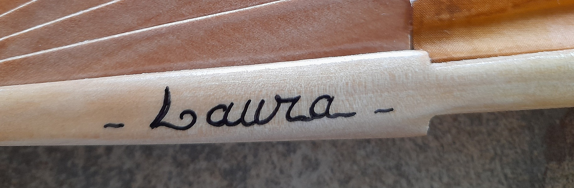Signature artisanale Nana gravée sur une branche d'éventail en bois.