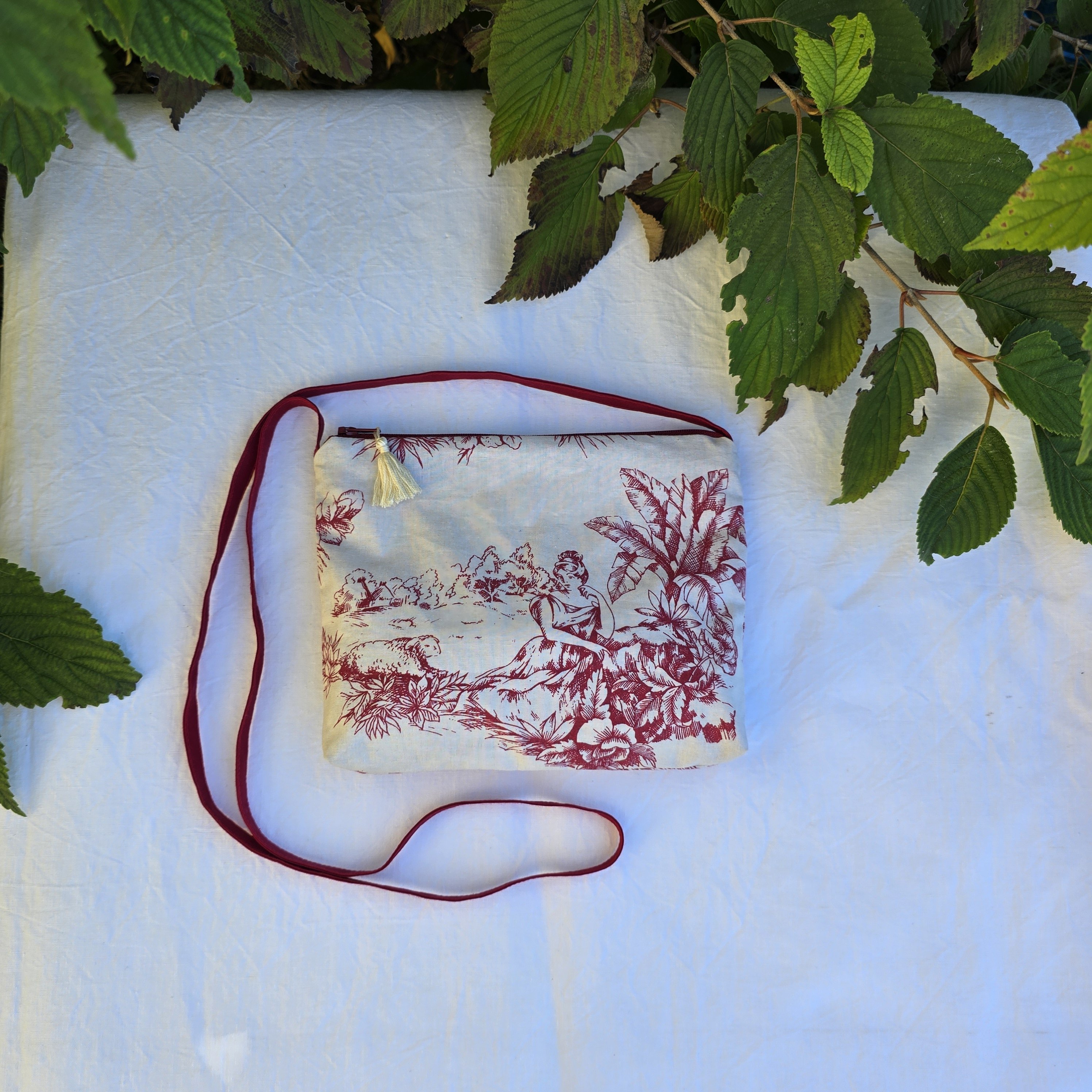 Pochette avec bandoulière en tissu toile de Jouy bordeaux et écru agrémentée d'un pompon