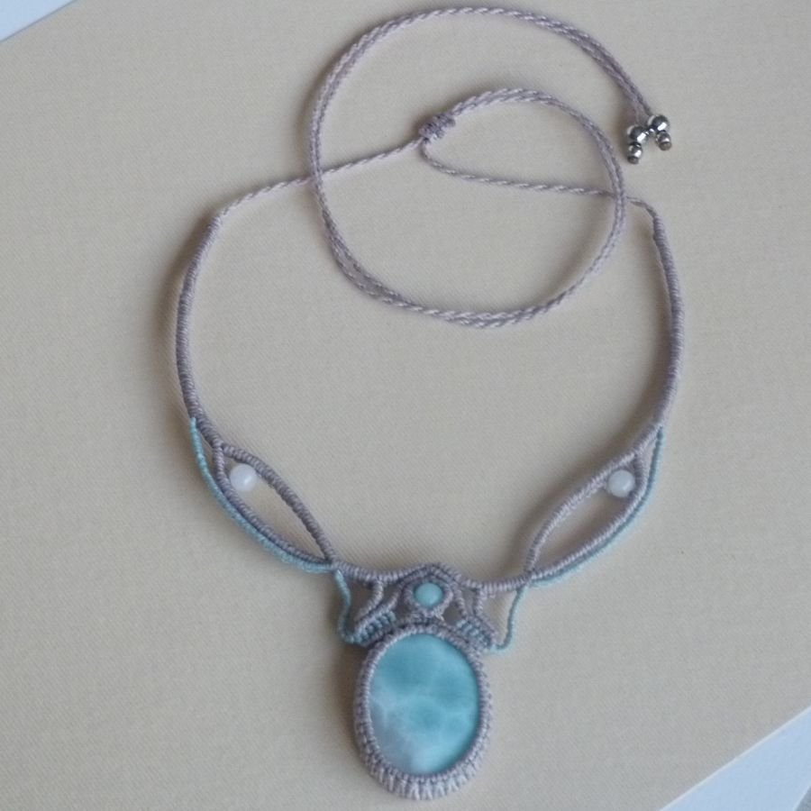 Necklace in taupe gray/frosted blue micro-macramé with a natural gemstone in soft shades of white and light blue in the center.