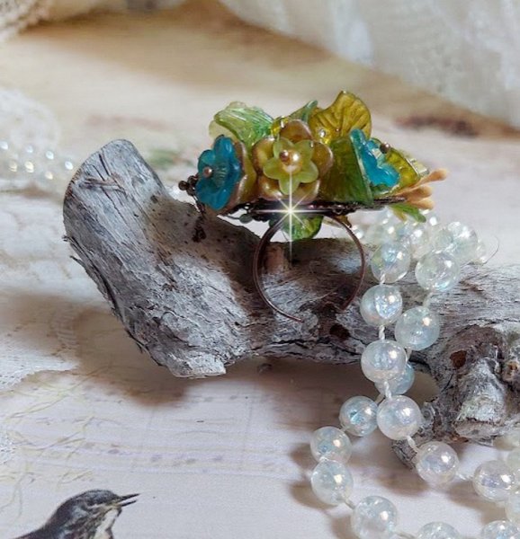 Bague Cézanne montée avec des petites fleurs lucites peintes à la main à laquelle s’ajoute des feuilles, cristaux, perles, étamines, grosses rocailles, perles nacrées et métal sur une bague en Laiton