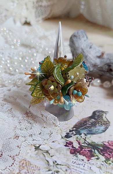 Bague C&eacute;zanne mont&eacute;e avec des petites fleurs lucites peintes &agrave; la main &agrave; laquelle s&rsquo;ajoute des feuilles, cristaux, perles, &eacute;tamines, grosses rocailles, perles nacr&eacute;es et m&eacute;tal sur une bague en Laiton