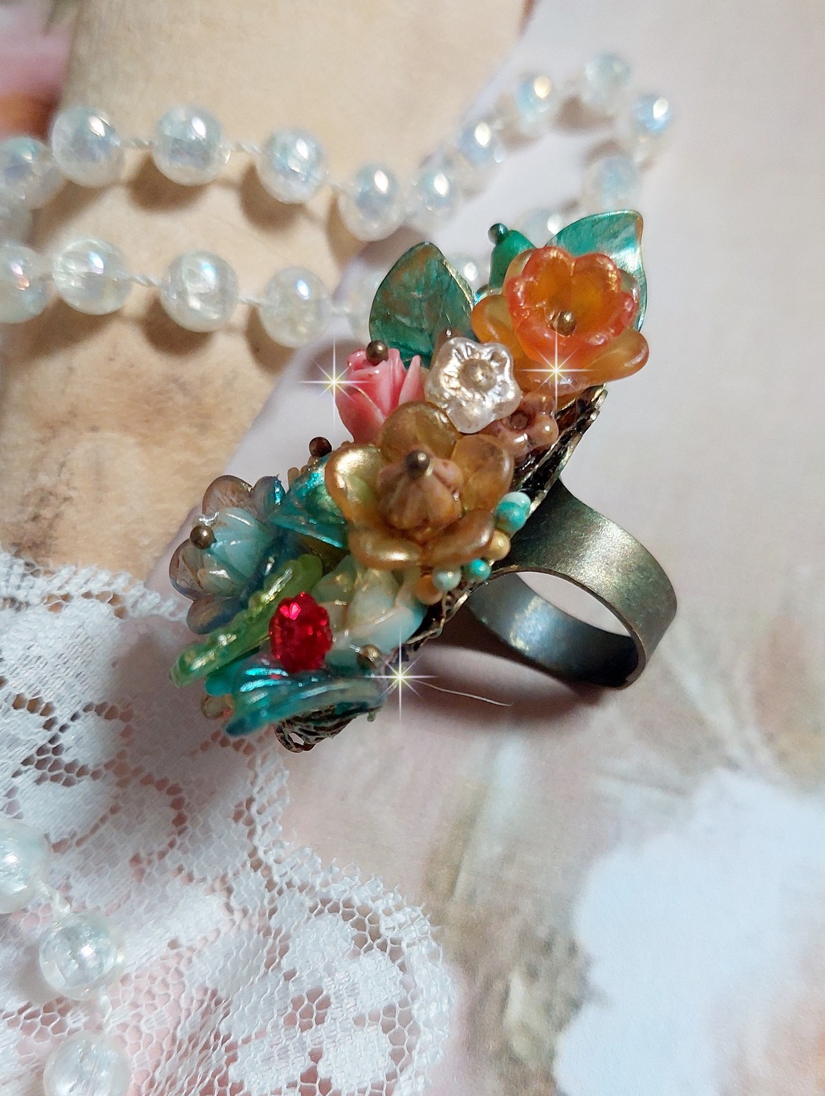 Bague Patiflo d’une composition florale créée avec des cristaux, fleurs en Résine, perles, clochettes, pensées, boutons de rose en Verre, estampes et coupelles. Le tout est monté sur une bague estampe