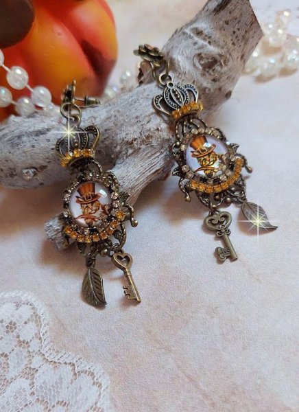 BO Chatibo Steampunk mont&eacute;es avec cabochons ronds en verre repr&eacute;sentant un chat chapeaut&eacute; Haute de Forme Orange. Strass&eacute;es avec une couronne, breloques cl&eacute;s et feuilles. Mont&eacute;es sur clips Bronze