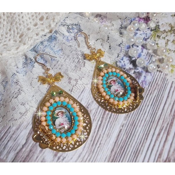 BO Mademoiselle Noellia avec des cabochons ovales repr&eacute;sentant une femme avec un chapeau et un n&oelig;ud blanc &agrave; laquelle s&rsquo;ajoute des cristaux, cha&icirc;nes strass P&ecirc;che et Turquoise sur crochets en plaqu&eacute; Or