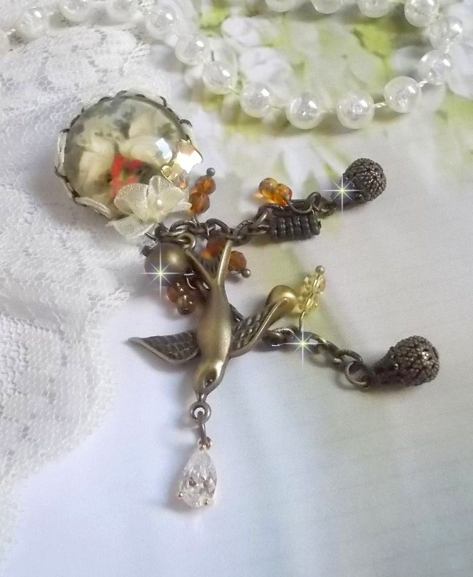 Broche Colombes aux plumages blancs avec des breloques filigranées gouttes et lisses, perles rondes et nœud en cristal, ruban organza crème, pendentif plaqué or avec un zircon sur une broche en métal