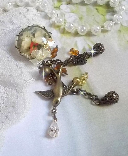 Broche Colombes aux plumages blancs avec des breloques filigran&eacute;es gouttes et lisses, perles rondes et n&oelig;ud en cristal, ruban organza cr&egrave;me, pendentif plaqu&eacute; or avec un zircon sur une broche en m&eacute;tal