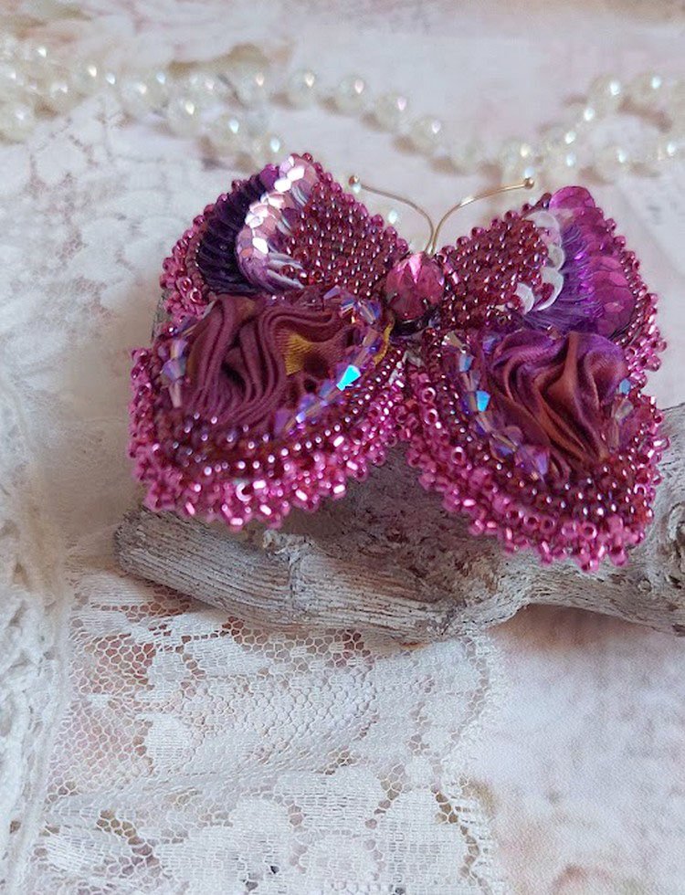 Broche Papillon Violine Fuchsia brodée avec un ruban de soie Fuchsia, Rose et Bordeaux à laquelle s’ajoute une navette sertie, des toupies en Cristal de Swarovski, sequins pailletés et rocailles