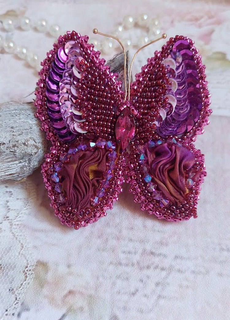 Broche Papillon Violine Fuchsia brodée avec un ruban de soie Fuchsia, Rose et Bordeaux à laquelle s’ajoute une navette sertie, des toupies en Cristal de Swarovski, sequins pailletés et rocailles