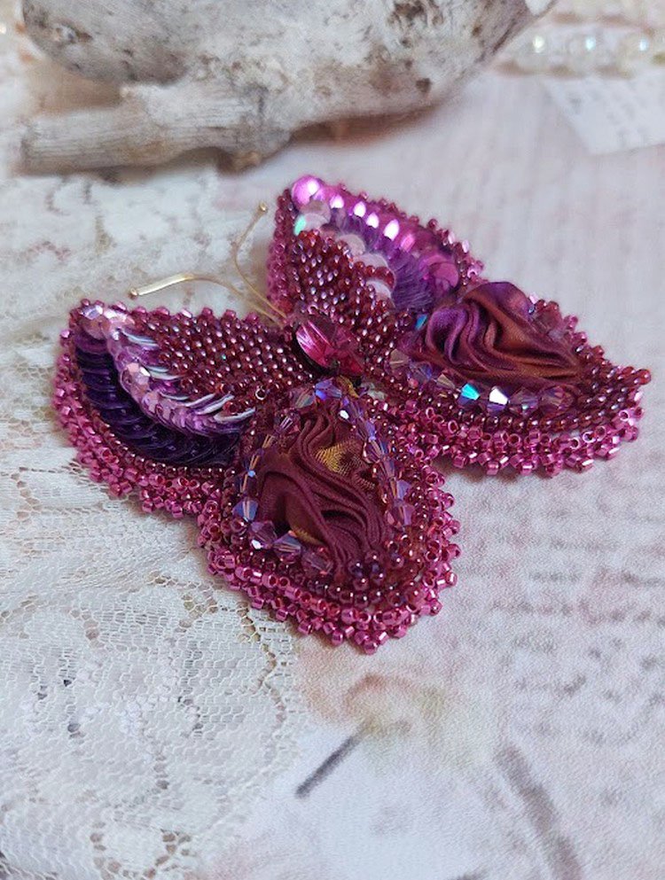 Broche Papillon Violine Fuchsia brodée avec un ruban de soie Fuchsia, Rose et Bordeaux à laquelle s’ajoute une navette sertie, des toupies en Cristal de Swarovski, sequins pailletés et rocailles