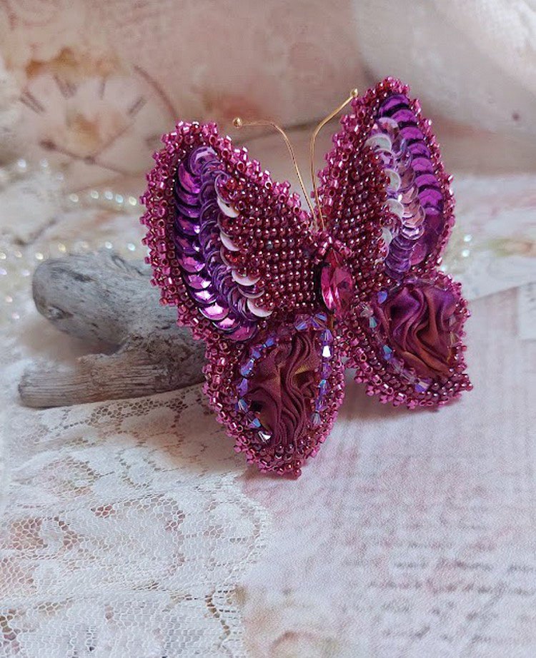 Broche Papillon Violine Fuchsia brodée avec un ruban de soie Fuchsia, Rose et Bordeaux à laquelle s’ajoute une navette sertie, des toupies en Cristal de Swarovski, sequins pailletés et rocailles