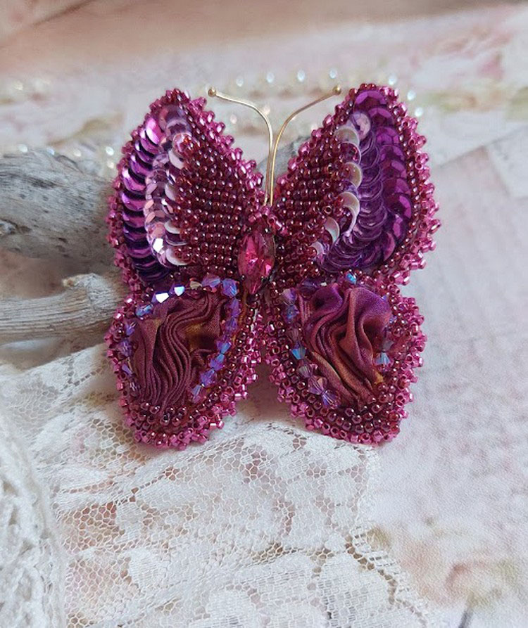 Broche Papillon Violine Fuchsia brodée avec un ruban de soie Fuchsia, Rose et Bordeaux à laquelle s’ajoute une navette sertie, des toupies en Cristal de Swarovski, sequins pailletés et rocailles