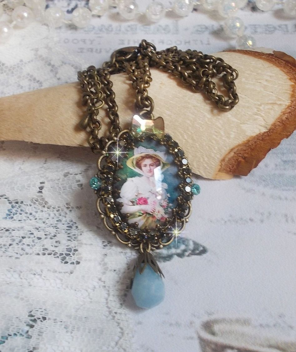 Pendentif Douce Dame créé avec un cabochon représentant une femme au chapeau blanc orné de cristaux, des accessoires de couleur Bronze et un jade teinté bleu 